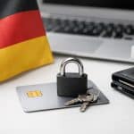 Kreditkarte auf einem Schreibtisch mit Vorhängeschloss und Schlüsseln darauf, daneben eine deutsche Flagge, eine Geldbörse und ein Laptop mit Sicherheitssymbol im Hintergrund. Das Bild vermittelt das Thema Deutschland und Kreditkartensicherheit und zeigt Gewohnheiten, die Risiken reduzieren können, wie Schutzmaßnahmen und verantwortungsvolle Nutzung einer Kreditkarte im digitalen Zahlungsverkehr.