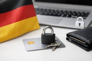 Kreditkarte auf einem Schreibtisch mit Vorhängeschloss und Schlüsseln darauf, daneben eine deutsche Flagge, eine Geldbörse und ein Laptop mit Sicherheitssymbol im Hintergrund. Das Bild vermittelt das Thema Deutschland und Kreditkartensicherheit und zeigt Gewohnheiten, die Risiken reduzieren können, wie Schutzmaßnahmen und verantwortungsvolle Nutzung einer Kreditkarte im digitalen Zahlungsverkehr.